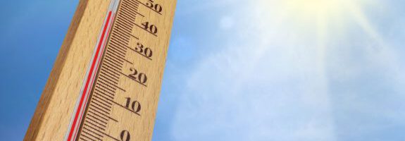 Thermometer zeigt Hitze an vor blauem Himmel mit Sonnenschein