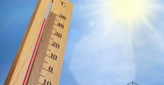 Thermometer zeigt Hitze an vor blauem Himmel mit Sonnenschein