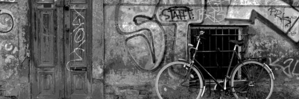 Ein schwarz-weiß Bild einer Hausfassade mit Graffiti und einem Fahrrad