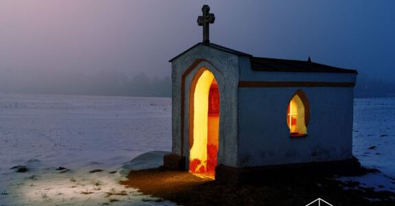 Eine Kapelle im Schnee bei Nacht, die von innen beleuchtet ist